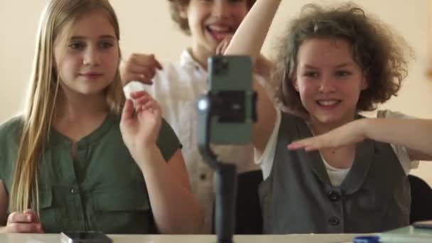 Söta skolflickor och skolpojkar spela in video på en smartphone kamera. Tonåringar fångar trender sociala medier, influencers tonåringar i skolan i klassen. Video bloggning och berättelse koncept — Stockvideo