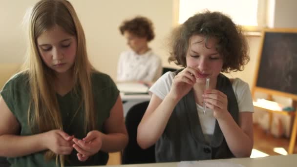 Two busy schoolgirls sit in school class. Their classmate is a curly-haired boy enjoys device free time — Stock Video