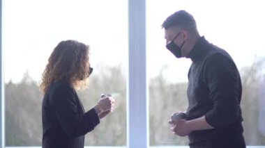 Maske takan, gülümseyen beyaz meslektaşların yakın çekimi ofis alanında birbirini selamladı. Modern ofiste kahve molası veren yaratıcı meslektaşlar. İş çifti iş birliği içinde konuşuyor.