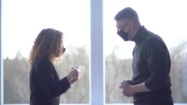 Close-up of smiling caucasian colleagues wearing masks greeted each other in office space. Creative colleagues having coffee break in modern office. Business couple talking in coworking — Stockvideo