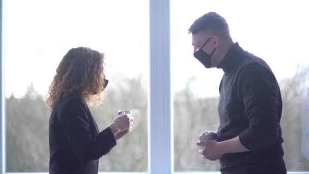 Close-up of smiling caucasian colleagues wearing masks greeted each other in office space. Creative colleagues having coffee break in modern office. Business couple talking in coworking — стоковое видео