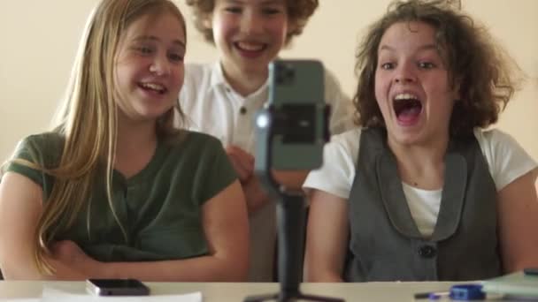 Två flickor och en lockig pojke klasskamrater tittar på en rolig video i en smartphone i skolan under en paus. Begreppet trender i sociala medier — Stockvideo