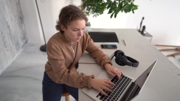 Beautiful 13 years old blond girl in glasses sitting at the desk doing her homework using a laptop. — Stock Video