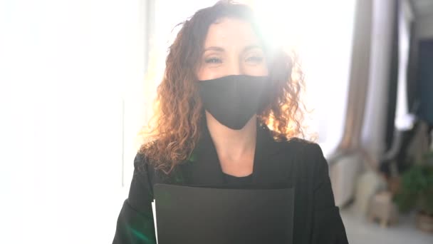 Focused business woman in disposable black face mask holds a folder with documents in his hands in office. Preventions of viral infection spread. New rules during the COVID-19 pandemic