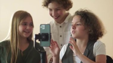 Three schoolchildren are filming a video using a smartphone and a steadicam. Two girls and a boy, funny classmates shoot video trends