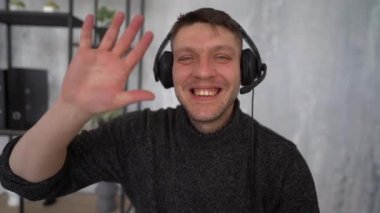 Happy smiling young man looking at camera and speaking. Wave his hand in greeting during video call. Using modern communication technology