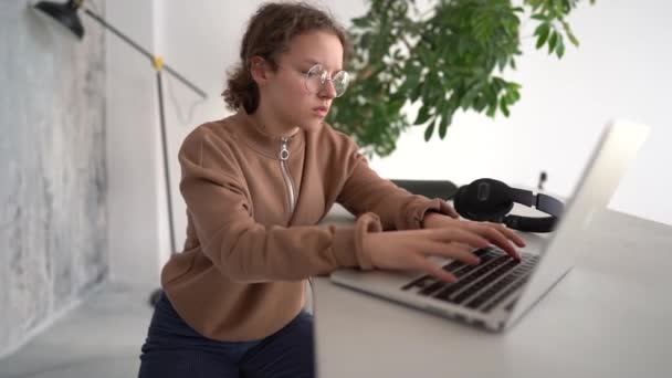 Side view of serious teen girl working with laptop in coworking space. Doing homework, chatting with friends on social networks, surfing the Internet — стоковое видео