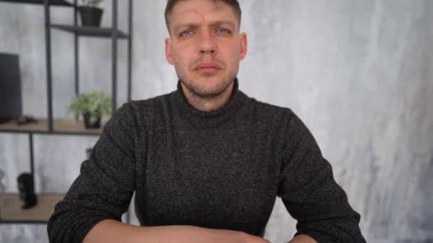 Portrait of a serious adult Caucasian man in a gray sweater sitting at a table in the office. Employee, middle age — Vídeo de Stock