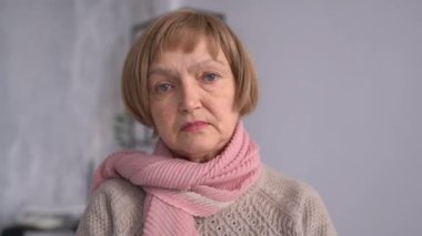 Portrait of senior lady. Close-up indoor portrait of sad old woman with short hair and pink scarf. Stylish mature woman alone