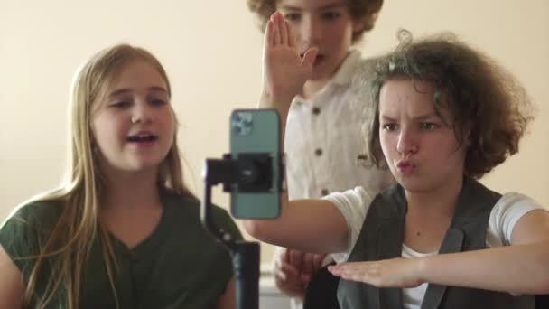 Two girls and a boy, funny classmates shoot video trends. Three schoolchildren are filming a video using a smartphone and a steadicam — Vídeo de Stock