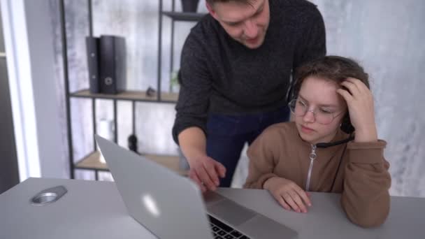 Ojciec odpowiada na pytania córek, pokazując je na ekranie laptopa. Nastolatka uczy się zdalnie i prosi rodzica o pomoc. Zdalne uczenie się, Dzień Ojca — Wideo stockowe