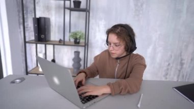 The face of a girl in headphones looking towards the laptop screen while studying remotely. Schoolgirl listens to lessons online