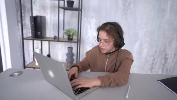 The face of a girl in headphones looking towards the laptop screen while studying remotely. Schoolgirl listens to lessons online — стоковое видео
