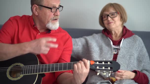 Retrato de una pareja de ancianos disfrutando tocando la guitarra en su propia casa. Tienen una cara sonriente y feliz. Concepto de actividad de la edad de jubilación — Vídeo de stock