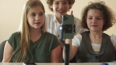 Children and teenagers watch videos and repeat dances in front of a smartphone camera. Schoolchildren and smartphone in class