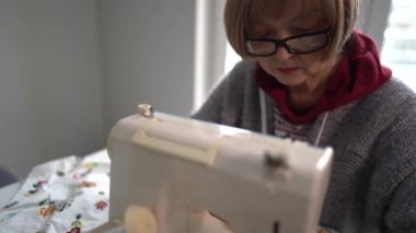 Elderly gray-haired woman scribbles on a typewriter. Small business and home hobby concept. Remote employment