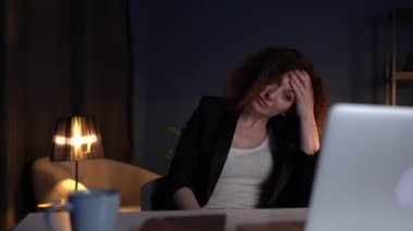 Working difficulties and overworking concept. Mature attractive woman in a black business suit is working in the office late at night
