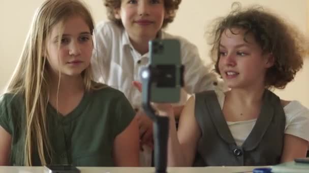 Baile alegre delante de un teléfono inteligente, las niñas y un niño se divierten filmando videos para redes sociales, video blogging entre los escolares — Vídeo de stock