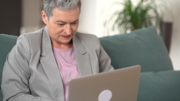 快乐的老太太奶奶在家里用笔记本电脑。漂亮而快乐的女商人，剪短发，离家很远地工作 — 图库视频影像