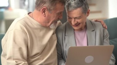 Güzel bir çift, bir erkek ve bir kadın, evdeki kanepede yan yana otururken internette video izlerken eğleniyorlar.