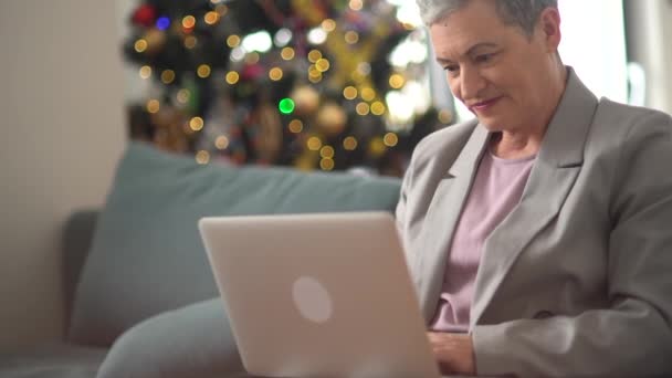 Ένας στοργικός ηλικιωμένος έφερε μια κούπα τσάι σε μια γκριζομάλλα γυναίκα ενώ αυτή καθόταν στον καναπέ. Παντρεμένο ζευγάρι γιορτάζει Χριστούγεννα — Αρχείο Βίντεο