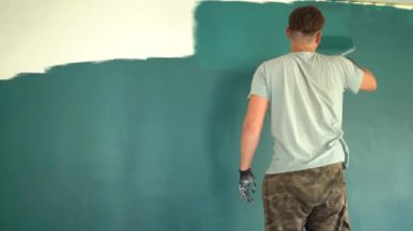 Bir adam silindirle duvar boyuyor. Odada tamirat yapan bir adam. Modern iç mekan. Güzel tasarım. Kendini soyutlama. Karantinaya alın. Yüksek kaliteli onarım