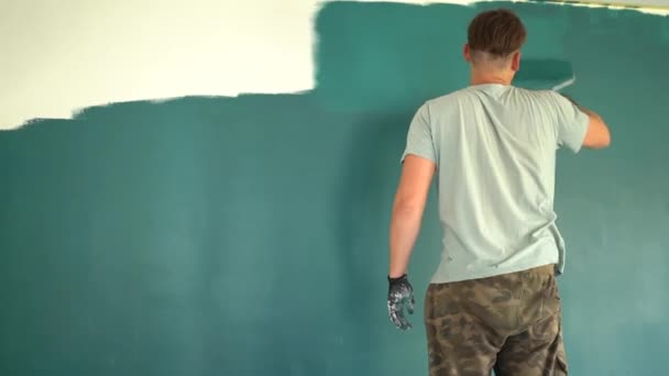 Um homem pinta uma parede com um rolo. Um homem faz reparações na sala. Interior moderno na casa. Belo design. Auto-isolamento. Quarentena. Reparos de alta qualidade — Vídeo de Stock