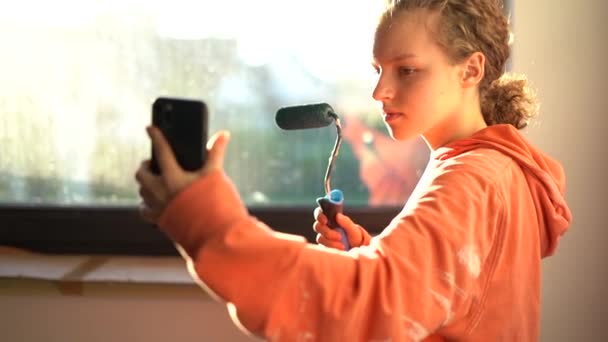 Słodka dziewczyna z rolki farby w rękach robi selfie podczas malowania ścian w jej pokoju. Koncepcja mediów społecznościowych i młodzieży — Wideo stockowe