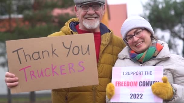 Reunião de apoio aos protestos anti-vacinação no Canadá em Ottawa. Um homem e uma mulher com roupas quentes seguram cartazes com as inscrições obrigado caminhoneiros e comboio de liberdade — Vídeo de Stock