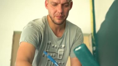 Gök mavisi bir tekerlekle duvar boyayan bir erkek işçi portresi. Tesis yenileme konsepti, inşaat işi