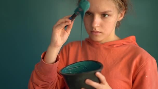 看着画从画笔上掉下来的青少年.卷曲的红头发姑娘，手里拿着刷子和一碗蓝色油漆。创造性和革新概念 — 图库视频影像