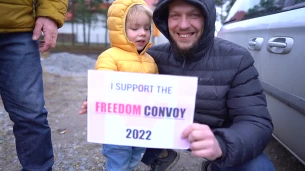 Retrato de um homem em uma jaqueta quente com um pequeno filho segurando um cartaz Eu apoio o comboio da liberdade 2022. Acção de apoio ao movimento contra a vacinação obrigatória no Canadá — Vídeo de Stock