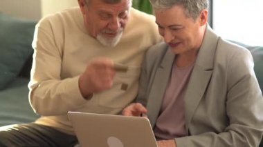 Kredi kartı ve dizüstü bilgisayarla online ödeme yaparken yaşlı çiftin konuştuğu orta ölçekli bir fotoğraf. Coronavirus karantina kilidi