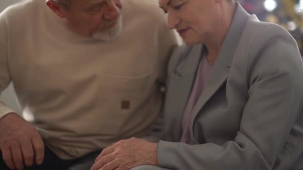 Triste anciana se sienta en un sofá, su marido se levanta y se consuela y abraza. Feliz familia madura — Vídeos de Stock