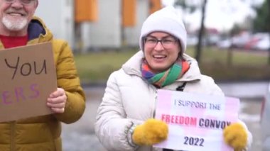 Kalın giysili bir kadın ve bir erkek yazıtlarla tabela tutuyorlar. Kamyoncular ve özgürlük konvoyu için teşekkürler. Kanada 'daki aşı karşıtı hareketi destekleyen gülümseyen insanların açık hava portresi
