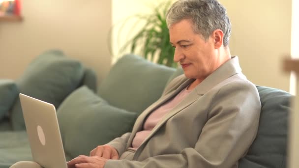Velha avó idosa feliz usando computador portátil em casa. Mulher de negócios feliz bonita com corte de cabelo curto trabalhando remotamente de casa — Vídeo de Stock