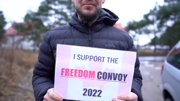Zbliżenie młodego człowieka w czarnej kurtce z plakatem z napisem Wspieram konwój wolności. Protesty przeciwko obowiązkowemu szczepieniu w Kanadzie — Wideo stockowe