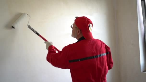 Vista trasera del hombre pintor mirando a la pared en blanco, con barra de rodillo de pintura, aislado en la habitación blanca — Vídeos de Stock