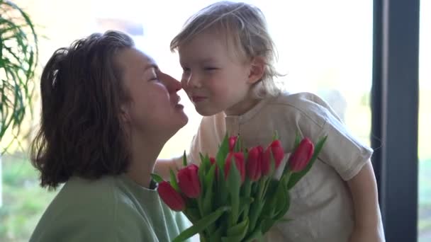 Niño le da a su madre un ramo de tulipanes rosados, felicitaciones en el día de las madres. Hijo de tres años de edad abraza y besa a su madre — Vídeo de stock