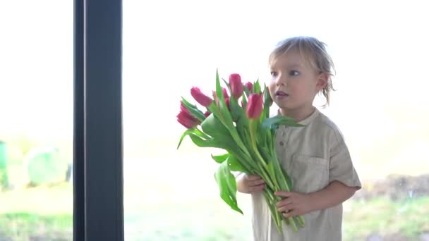 Mały, uroczy blondyn życzy swojej matce wszystkiego najlepszego i daje jej bukiet czerwonych tulipanów. Wiosenne wakacje i koncepcja Dnia Matki. Matka i syn — Wideo stockowe