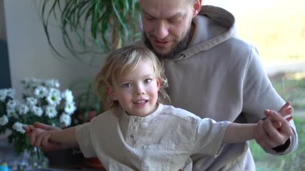 Glücklicher, fröhlicher Kaukasier, der seinen kleinen, niedlichen Sohn umarmt und zu Hause lacht. Fröhliche Eltern mit kleinem Kind im Wohnzimmer. Junger Vater lächelt und umarmt Kind drinnen. Vatertag — Stockvideo