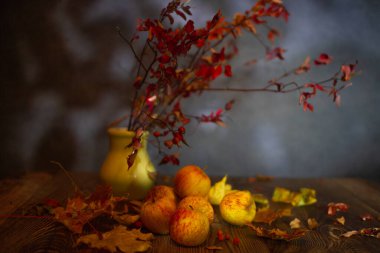 Solmuş elmalar, kuru yapraklar ve masada bir gül kalçası dalı.