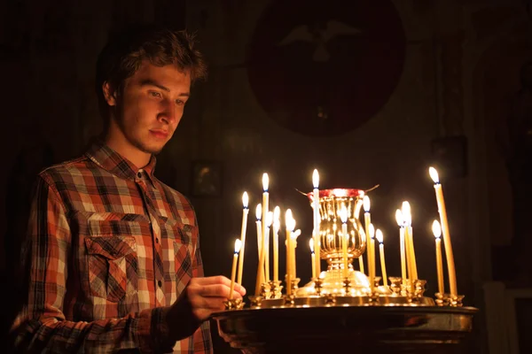 Young man lighting a candle in the church. — Stock Photo, Image