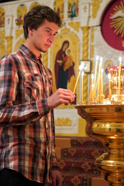 A fiatalember lighting a gyertya, az egyházban. — Stock Fotó