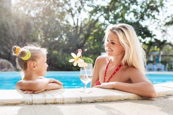Маленькая девочка и ее мать с коктейлем в тропическом бассейне — стоковое фото