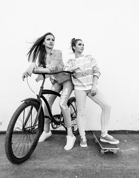 Two hipster girl friends with skateboard and bicycle. — Stock Photo, Image