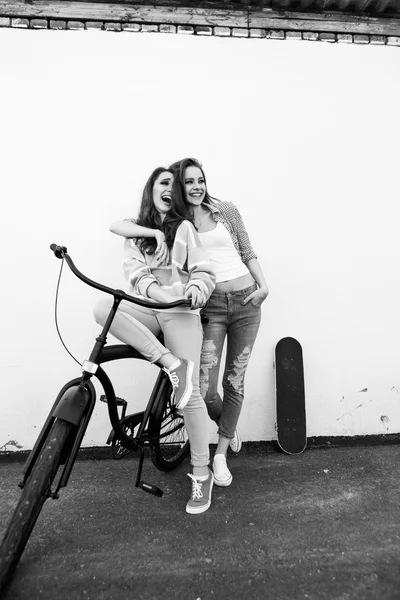 Two hipster girl friends  with skateboard and bicycle. — Stock Photo, Image