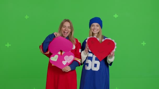 Two girlfriends are holding a paper poster and a heart-shaped card — Stockvideo