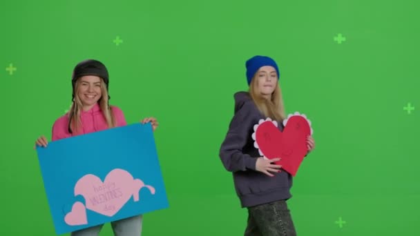 Two girlfriends are holding a paper poster and a heart-shaped card — Αρχείο Βίντεο