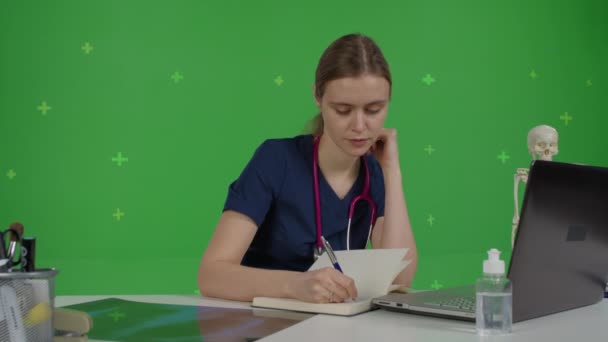 Biała kobieta lekarz na zielonym tle ekran siedzi przy stole — Wideo stockowe